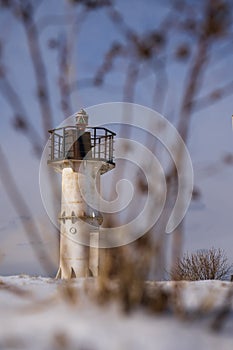 Old lighthouse in winter on a background of blue sky and bushes