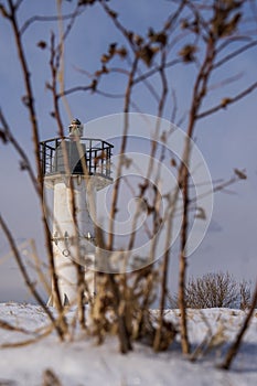 Old lighthouse in winter on a background of blue sky and bushes