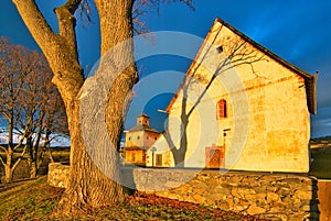 Old linden tree and stone wall around medieval church of St. Francis of Assisi in Poniky village