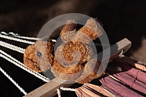 An old little brown plush bear lies next to a fabric hammock. The stuffed animal has obviously been forgotten and is lying on the photo