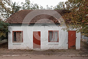 Old little shabby one-story white brick house with red doors and windows in the woods
