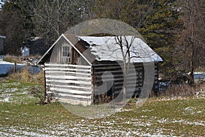Old log cabin storage building in the woods with light snow in winter