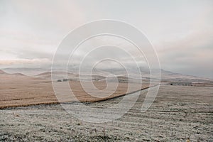 Old lonely house in field. Dawn in autumn field. Hills in morning haze. Grass covered with autumn hoarfrost. Nature in