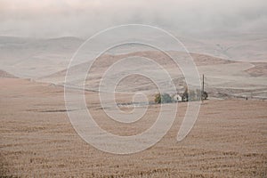 Old lonely house in field. Dawn in autumn field. Hills in morning haze. Grass covered with autumn hoarfrost. Nature in