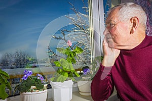 Old lonely man sitting near the window in his house.