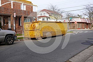 Old long yellow dumpster on an asphalt street in front of a brick building being renovated