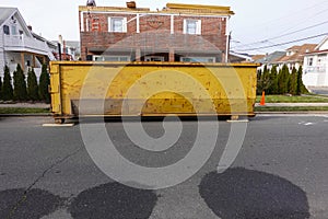 Old long yellow dumpster on an asphalt street in front of a brick building being renovated