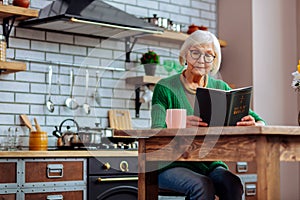 Old madam enjoying reading of Bible book at kitchen table