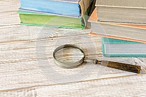 An old magnifying glass and a stack of books on a wooden table. The concept of getting knowledge from books. Selective focus