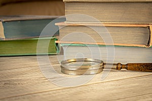 An old magnifying glass and a stack of books on a wooden table. The concept of getting knowledge from books. Selective focus