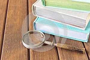 An old magnifying glass and a stack of books on a wooden table. The concept of getting knowledge from books. Selective focus