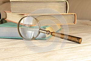 An old magnifying glass and a stack of books on a wooden table. The concept of getting knowledge from books. Selective focus