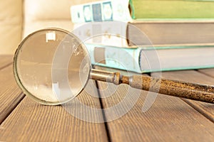 An old magnifying glass and a stack of books on a wooden table. The concept of getting knowledge from books. Selective focus