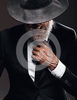 An old male actor playing an English spy role, hiding behind fedora hat.