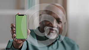 Old male African American biracial man at home sitting on couch businessman in office showing smartphone with empty