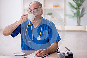 Old male doctor drinking coffee during break