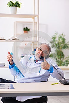 Old male doctor talking by telephone in the clinic