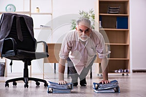 Old male employee doing physical exercises at workplace