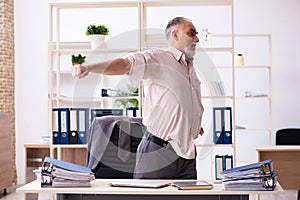 Old male employee doing physical exercises at workplace