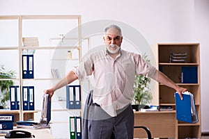 Old male employee doing physical exercises at workplace
