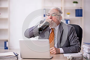 Old male employee drinking alcohol at workplace