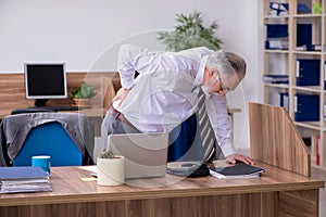 Old male employee suffering from radiculitis at workplace