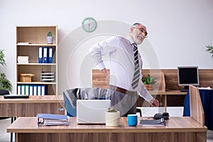 Old male employee suffering from radiculitis at workplace