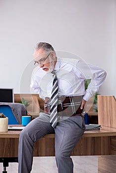 Old male employee suffering from radiculitis at workplace