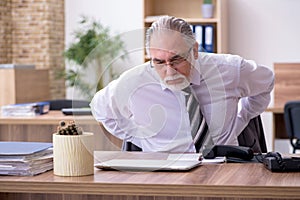 Old male employee suffering from radiculitis at workplace