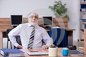 Old male employee suffering from radiculitis at workplace