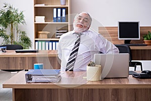 Old male employee suffering from radiculitis at workplace