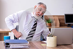 Old male employee suffering from radiculitis at workplace