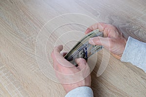 Old male hands hold paper dollars banknotes in his hands, counting a bundle of money, concept of cash, payments, savings
