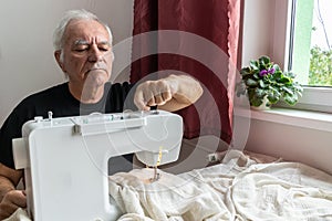 Old male man senior sit next at table at home work, sewing machine enjoy