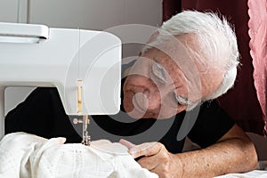 Old male man senior sit next at table at home work, sewing machine enjoy