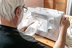 Old male man senior sit next at table at home work, sewing machine enjoy