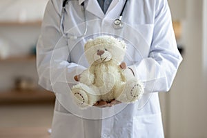 Old male pediatrician holding teddy bear in hands, close up