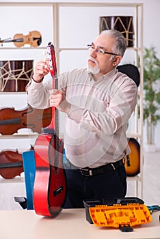 Old male repairman repairing musical instruments at workplace