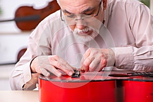 Old male repairman repairing musical instruments at workplace