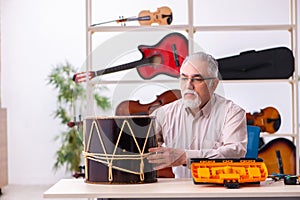 Old male repairman repairing musical instruments at workplace