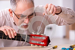 Old male repairman repairing musical instruments at workplace