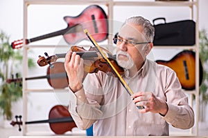 Old male repairman repairing musical instruments at workplace