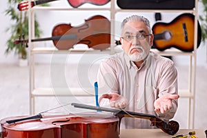 Old male repairman repairing musical instruments at workplace