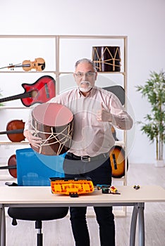 Old male repairman repairing musical instruments at workplace