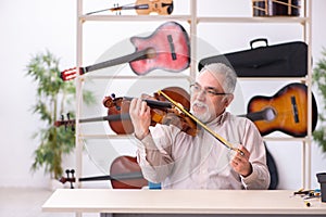 Old male repairman repairing musical instruments at workplace