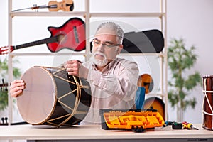 Old male repairman repairing musical instruments at workplace