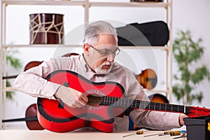 Old male repairman repairing musical instruments at workplace