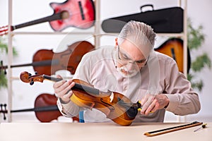 Old male repairman repairing musical instruments at workplace