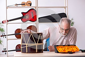 Old male repairman repairing musical instruments at workplace