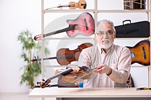 Old male repairman repairing musical instruments at workplace